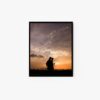 An enchanting art print titled untitled captures silhouettes of two people walking with fishing rods against a vibrant sunset sky, with distant mountains and a tranquil body of water forming a serene background.