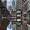 In Sheung Wan, a tram glides along tracks mirrored in a large puddle, skyscrapers loom under an overcast sky, and buildings line the street. The reflections beautifully capture the urban atmosphere with an art print quality that embodies modern life.