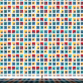 Someone walks past a large, colorful wall reminiscent of an art print—Tniy World—featuring a grid of windows with varied open shutters. Each window showcases red, yellow, blue, and green hues forming a vibrant geometric pattern.