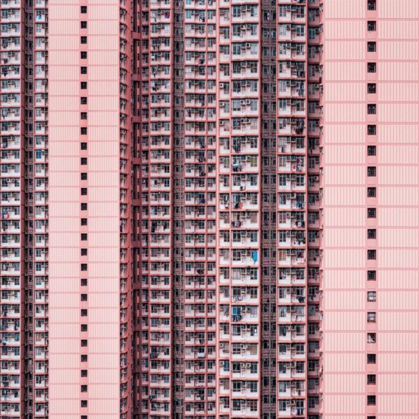 The tall residential building with a pink facade, named Density, features numerous balconies and uniform windows. Its repetitive architectural pattern evokes urban density and symmetry, reminiscent of an art prints meticulous design.