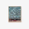 A tall, blue apartment building with many identical balconies fills the view like an art print titled Blue Frame. A solitary red car parked in front of the building creates a striking contrast against its repetitive architectural design.