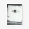 The abstract art print Inside the Blush Compact showcases a dreamy, introspective close-up of an eye and partial face in black and white. The soft focus, muted tones, and white frame emphasize the eyes detail and expression.