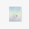 The art print Staring into Sunrise displays an eye centered in a clear droplet on a soft, pastel multicolored background. The serene design, framed in white, blends colors smoothly to create a dreamlike quality against a plain backdrop.