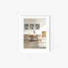 The Afternoon Coffee II art print shows a person seated at a long table reading in a serene, minimalist room. Behind them are three monochrome abstract portraits. Soft lighting creates gentle shadows, enhancing the calm atmosphere.