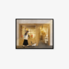 The art print titled A Trip to the Bookstore shows a woman in a skirt walking towards a warmly lit shop entrance with a cat following her. The Japanese text on the storefront adds charm, creating a cozy and inviting atmosphere.