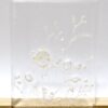 The Ever-blooming no.1(1) is a transparent resin block with delicate white floral patterns and small bubbles inside, resembling an exquisite art print. Its elegantly displayed on a light wooden surface against a plain white background.