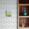 The wooden shelf displays a blue vase, glass vase, wooden mannequin, and small decorative item. On the adjacent wall, an art print complements the patterned wallpaper and features Pure, a small abstract painting with vibrant green and yellow hues.
