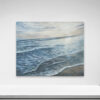 Shape of Water, 2018, beautifully captures a serene beach with gentle waves under a cloudy sky. Displayed on a white wall above a minimalist shelf, it adds tranquility to any space.