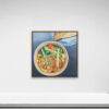 Square painting titled Veggies, 2021 features a colorful salad with tomatoes and cucumber in a wooden bowl, set on a white wall. A blue plate with bread is partially visible next to it. Displayed in a simple frame.